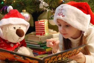クリスマスにくまのぬいぐるみと絵本を読む女の子